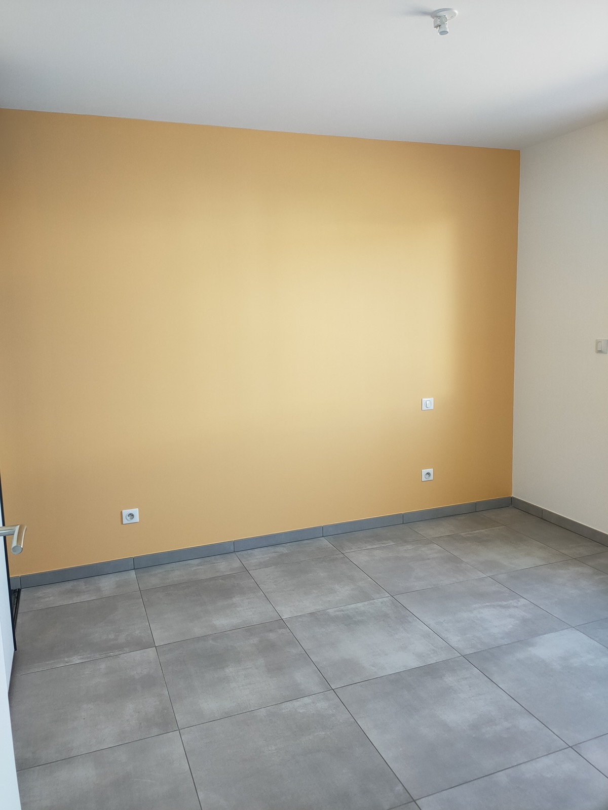 Pièce avec un mur peint en jaune ocre et carrelage gris, par la SARL VIDIEU